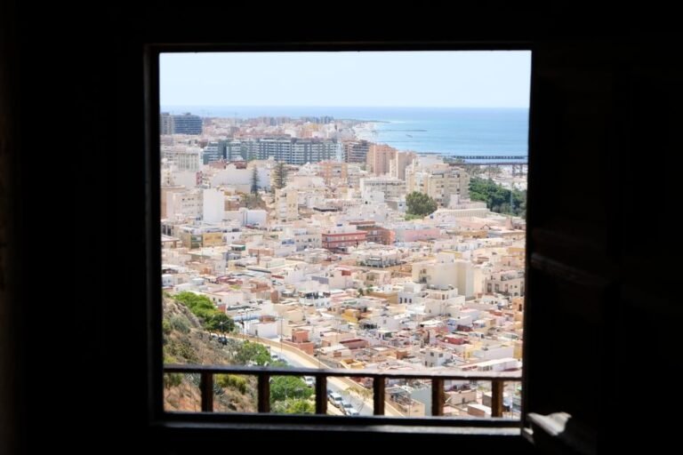 Vista aérea de una ciudad costera urbana a través del marco de una ventana, mostrando edificios y el mar.