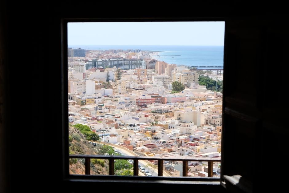 Vista aérea de una ciudad costera urbana a través del marco de una ventana, mostrando edificios y el mar.