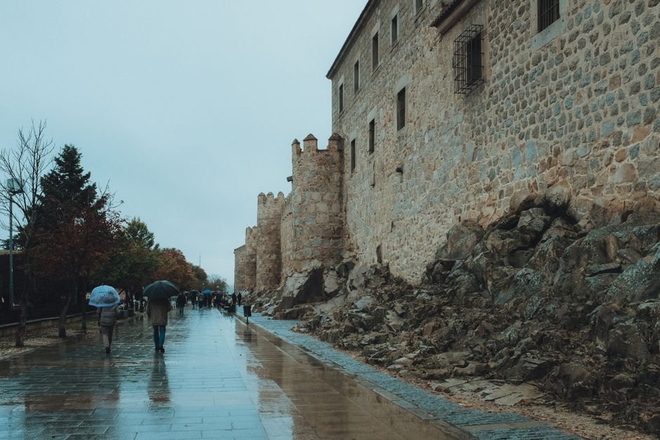 Gente caminando por calles mojadas junto a las antiguas murallas de Ávila, España.