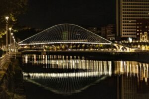 Vista nocturna del Puente Zubizuri iluminado en Bilbao reflejándose en la ría.