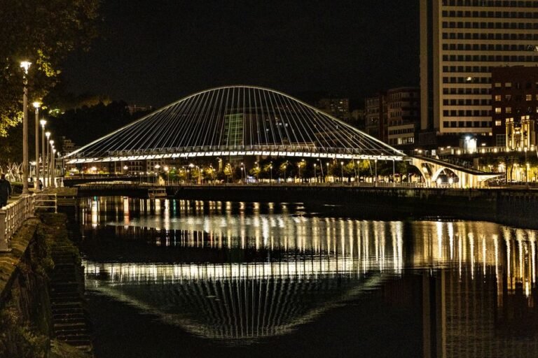 Vista nocturna del Puente Zubizuri iluminado en Bilbao reflejándose en la ría.